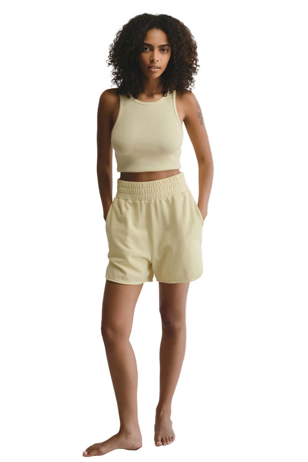 Woman wearing a light yellow sleeveless top and shorts against a white background