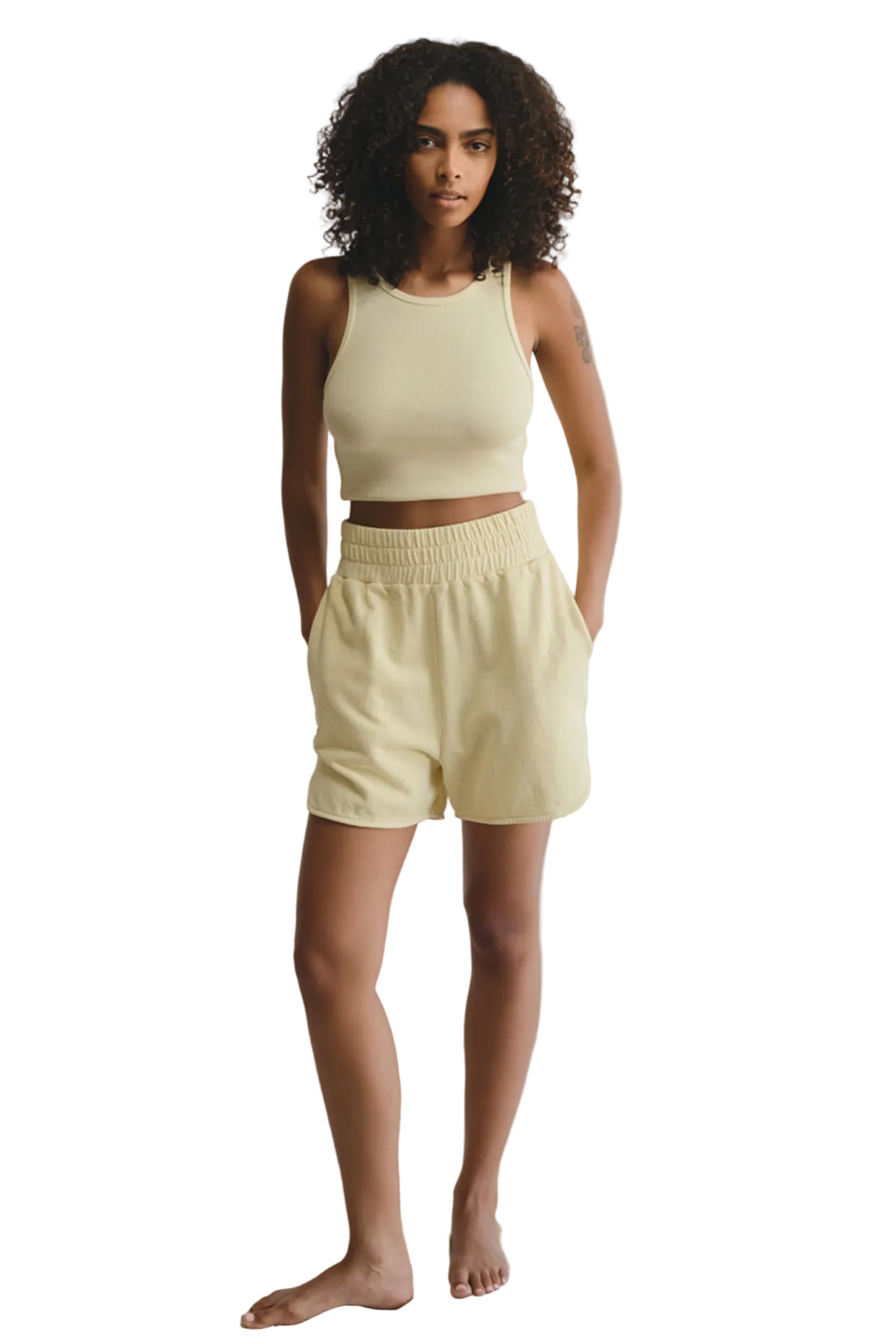 Woman wearing a light yellow sleeveless top and shorts against a white background