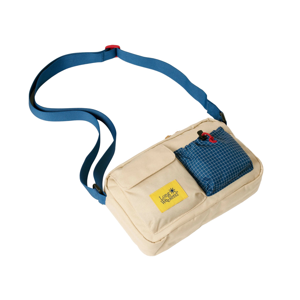 A beige crossbody bag with a blue strap, featuring a blue grid-patterned zippered pocket and a yellow 'JAPAN WALKER' brand patch on the front, set against a plain off-white background.