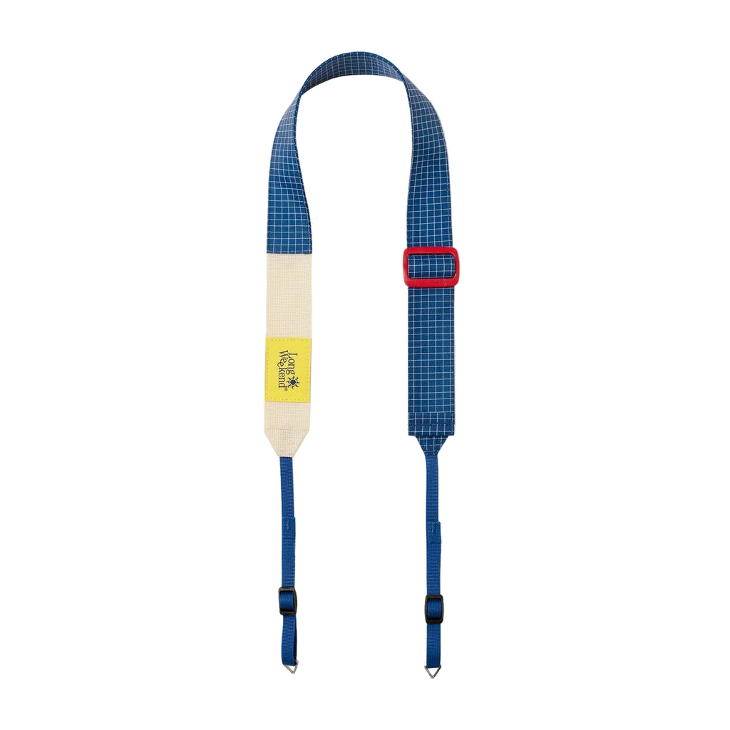 A blue and white checkered camera strap with a cream-colored center section, a small yellow brand patch, and a red buckle, displayed against a light gray background.