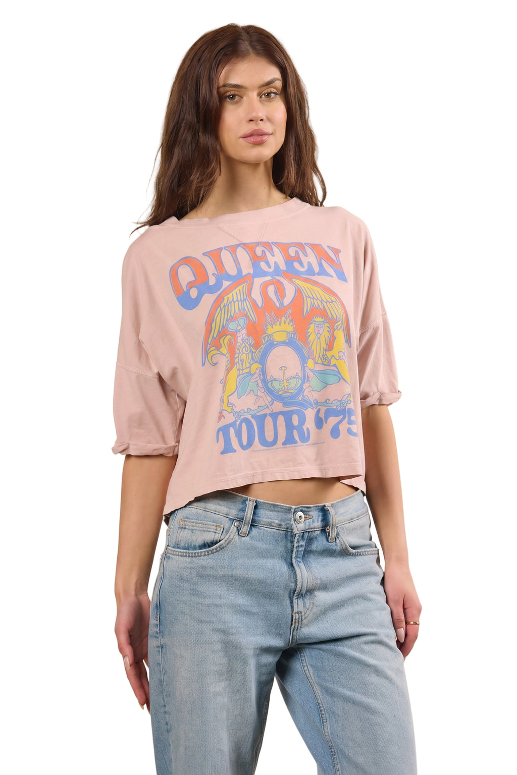 A woman modeling a light pink cropped graphic T-shirt with a colorful 'Queen Tour '76' print, paired with light-wash blue jeans against a solid white background.