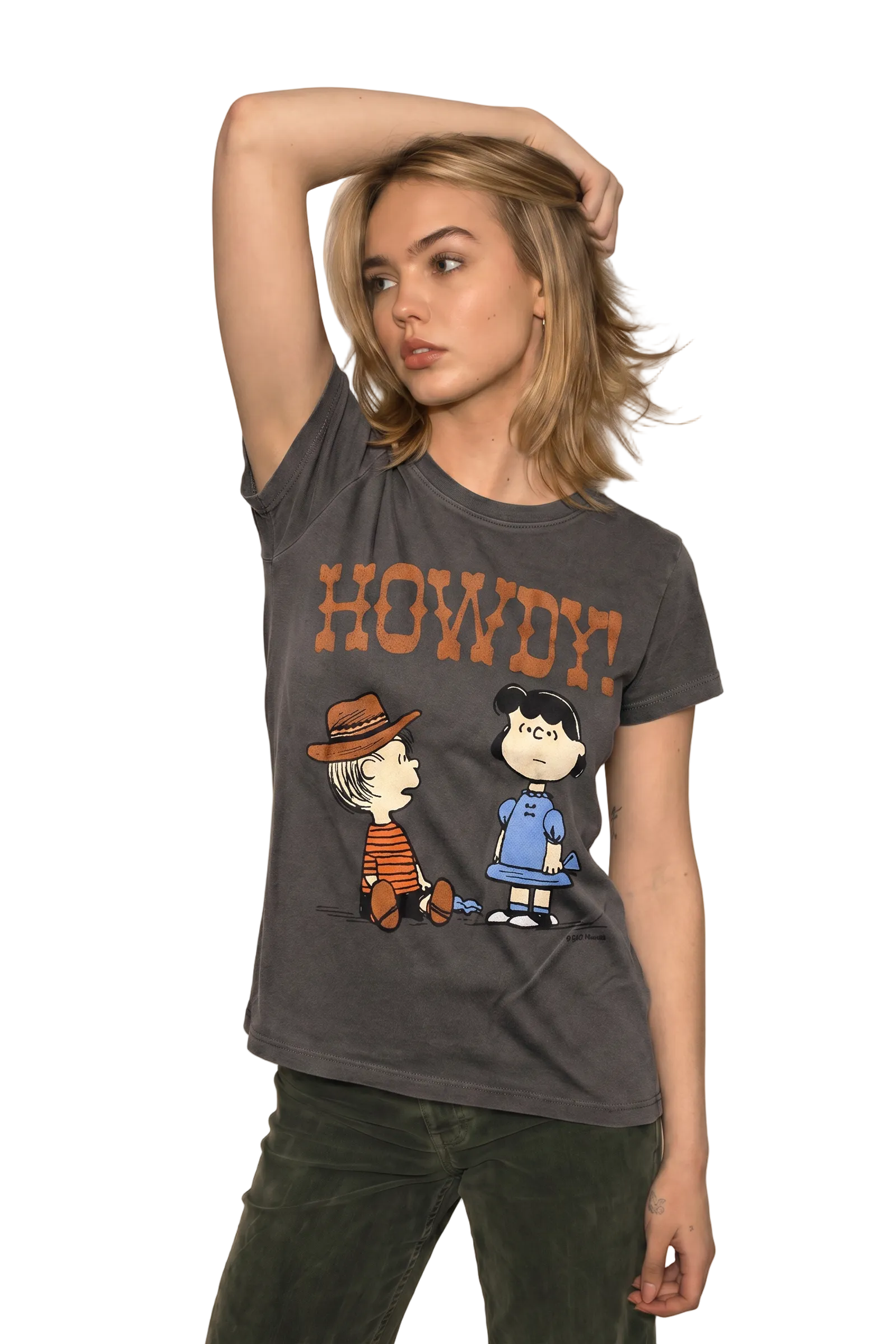 A woman modeling a dark gray graphic t-shirt featuring the text 'HOWDY!' and cartoon characters from Peanuts, paired with dark green pants, set against a solid beige background.