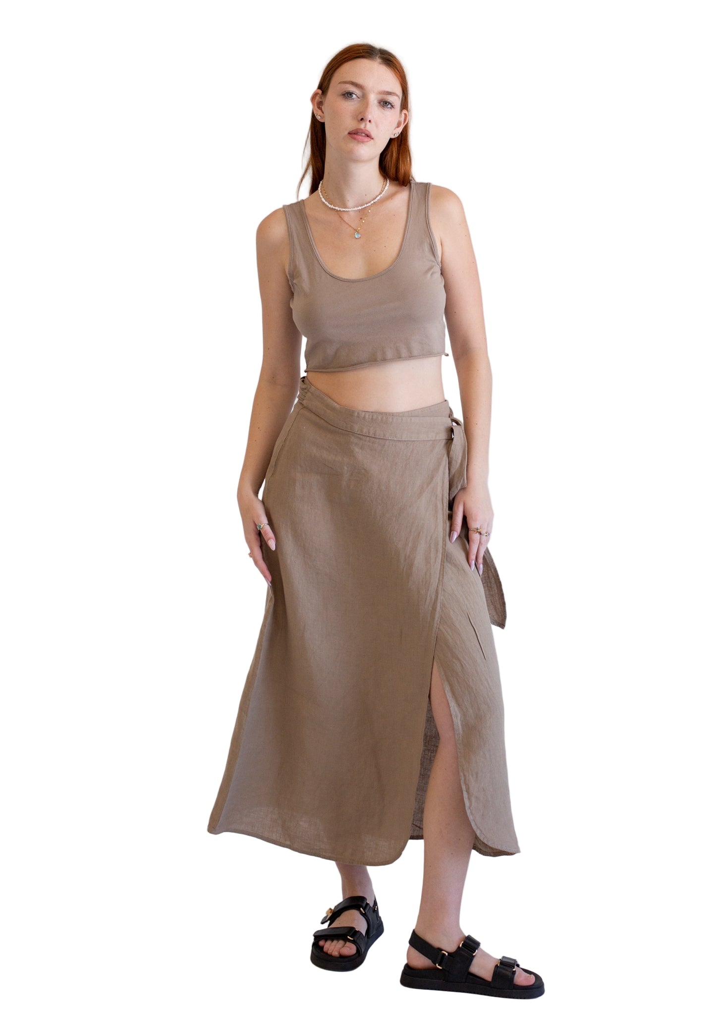 Woman wearing a beige tank top and long skirt against a white background