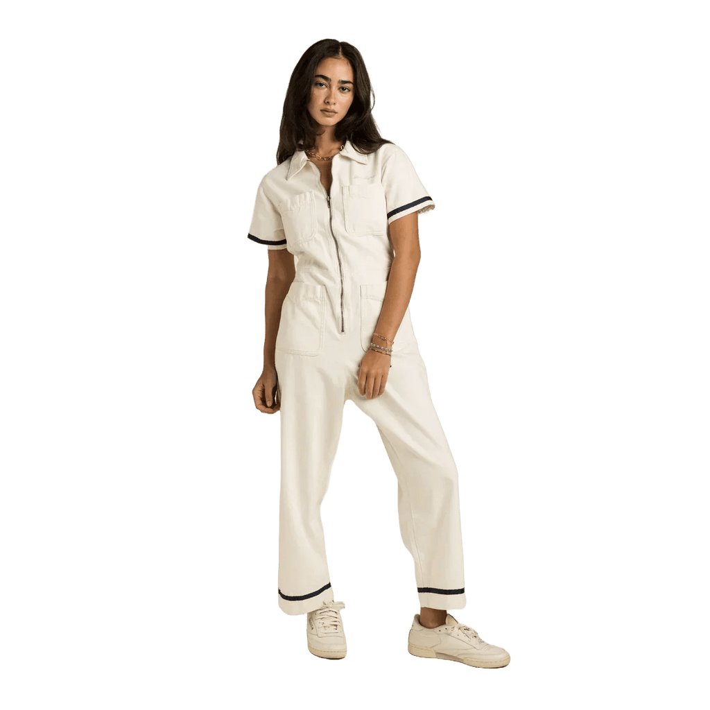 Sendero Dolly Jumpsuit in soft natural cotton ecru with navy tape accents and embroidered cream logo on chest pocket.