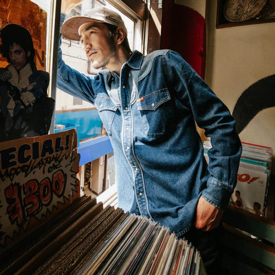 Model wearing Sendero Pearl Snap Denim Shirt in medium wash with western piping, pearl snaps, and classic cowboy style.