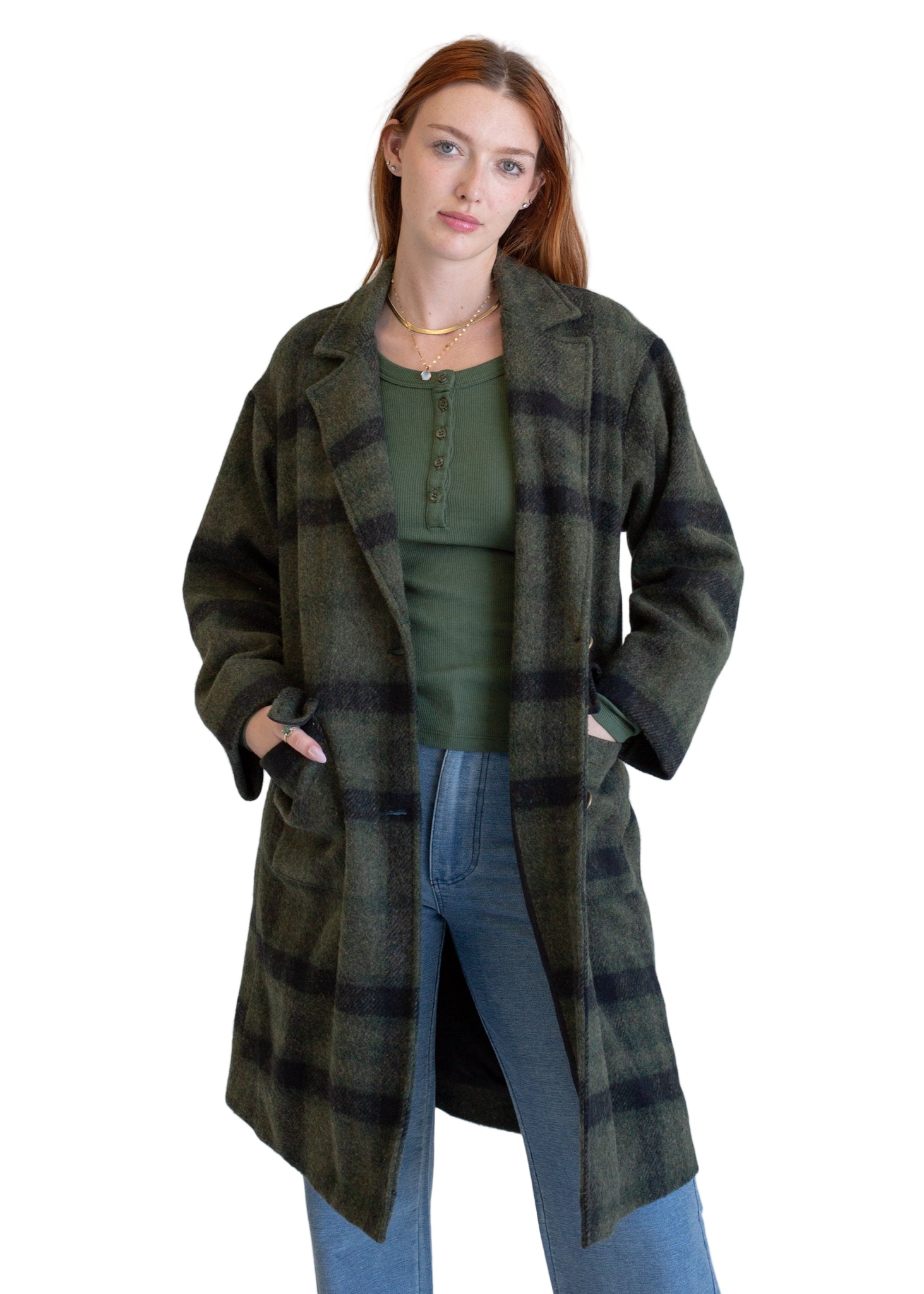 Woman wearing a green plaid coat over a green top and blue jeans on a white background